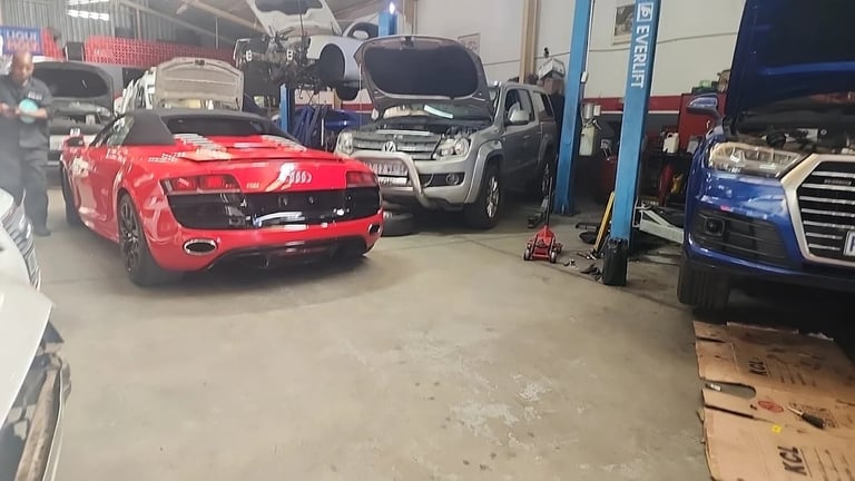 Red damaged sports car in an auto repair shop garage with other vehicles and equipment